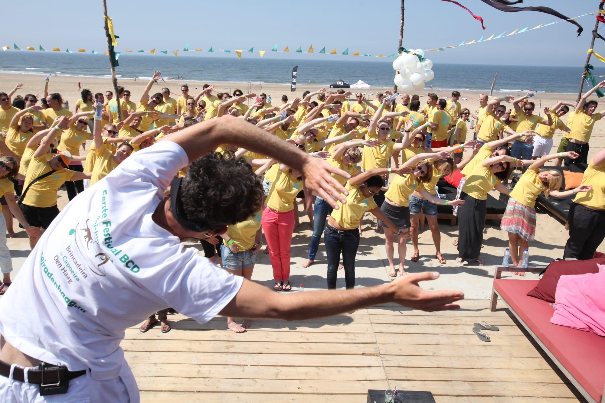 Vita leading a beach full of people through a warm-up at a festival